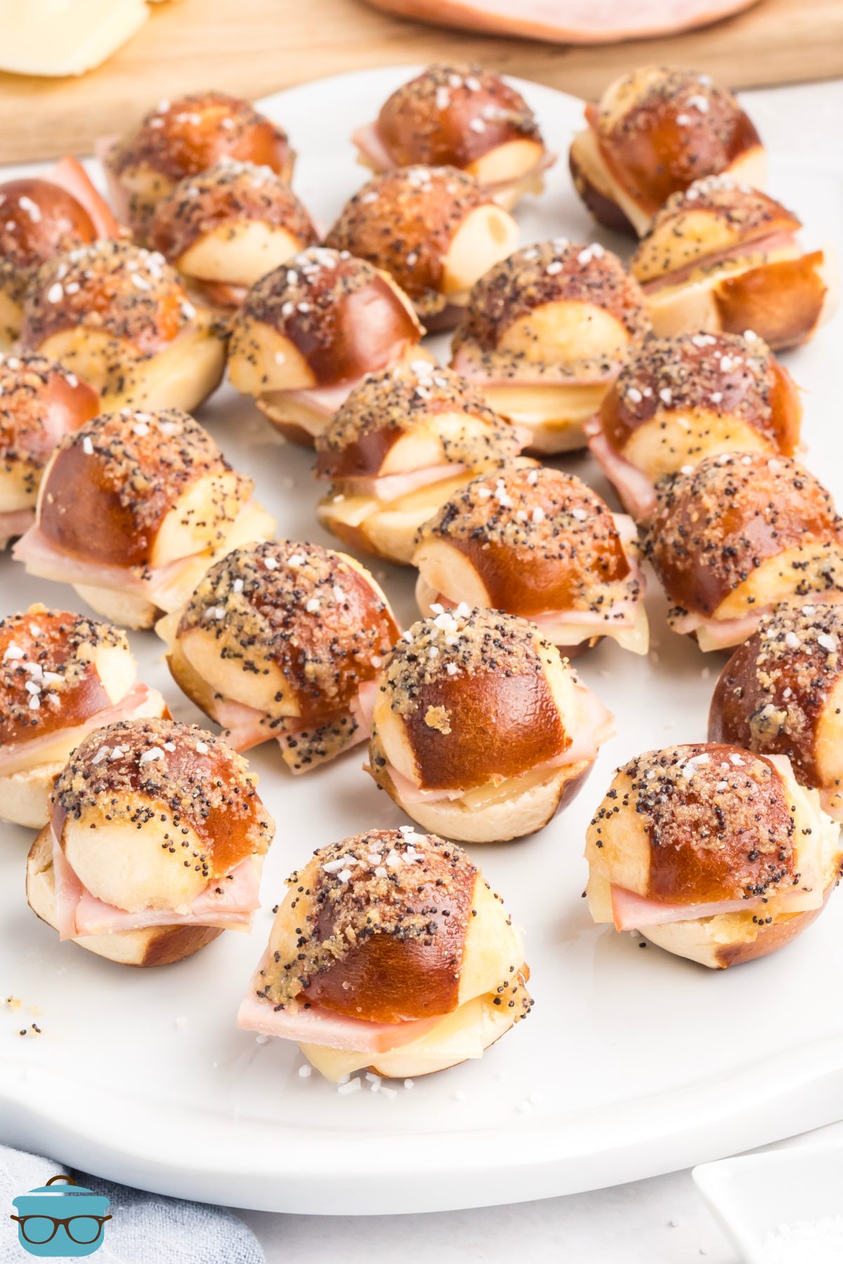 Ham and cheese pretzel bun sliders on a white serving platter.