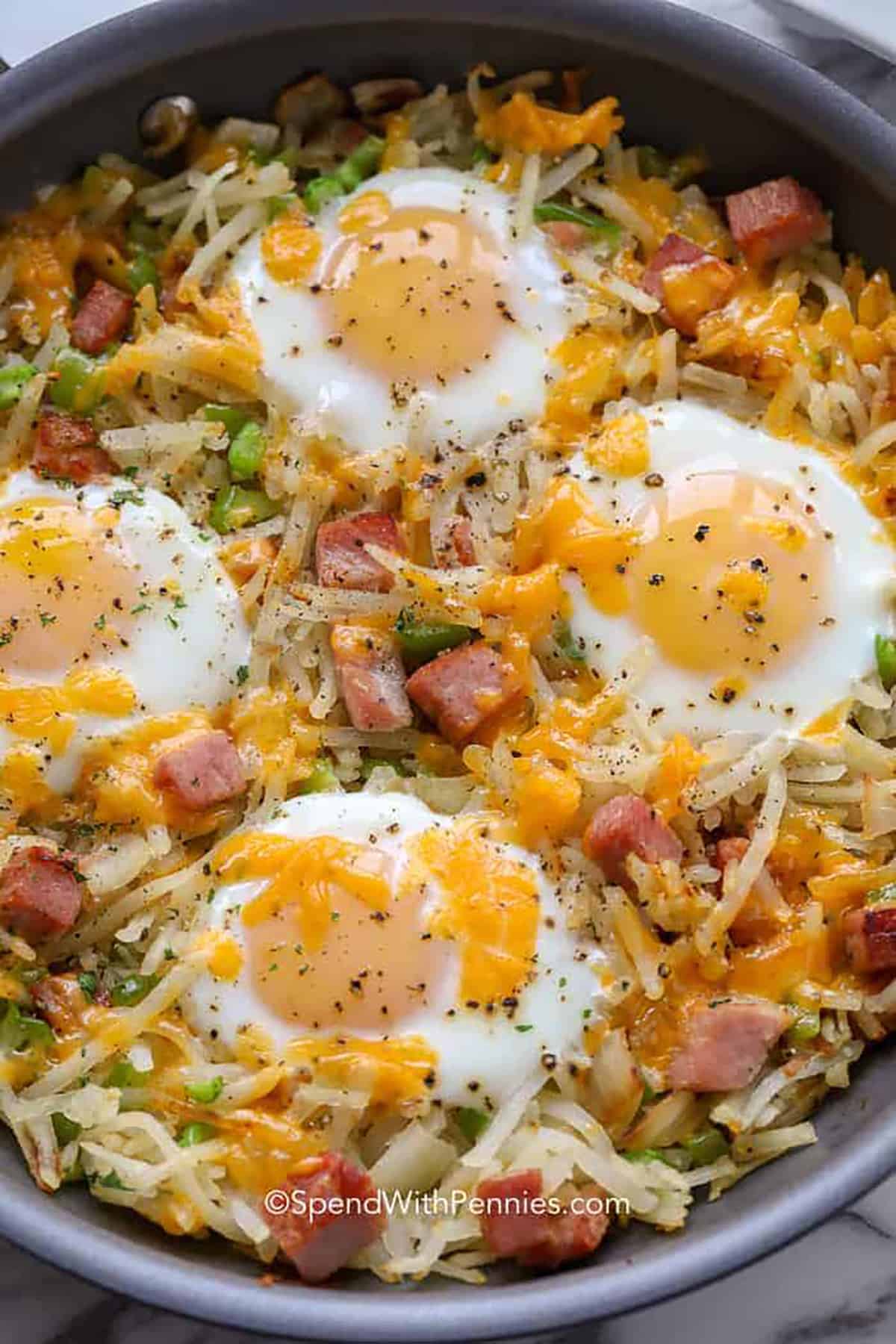 Ham breakfast hash with fried eggs on top in a skillet.