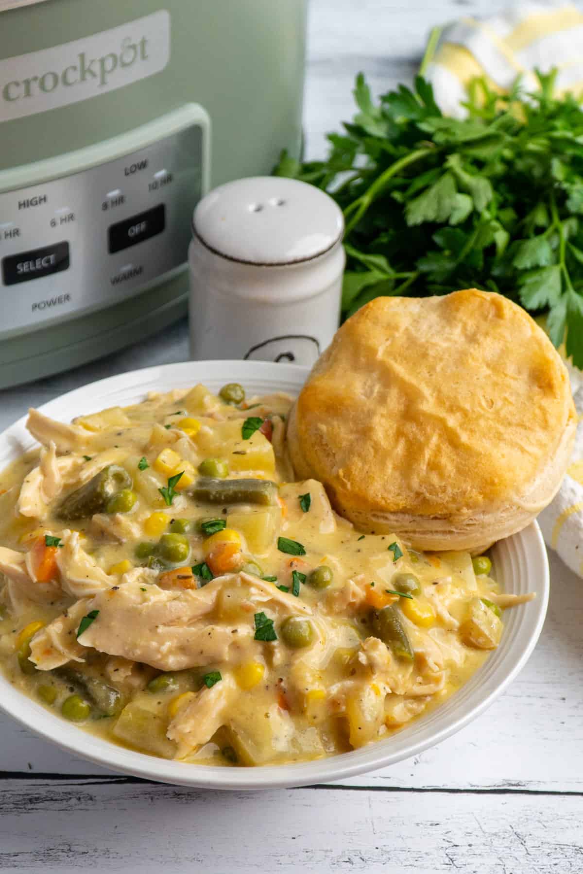 Crockpot chicken pot pie in a white bowl with a biscuit on top.
