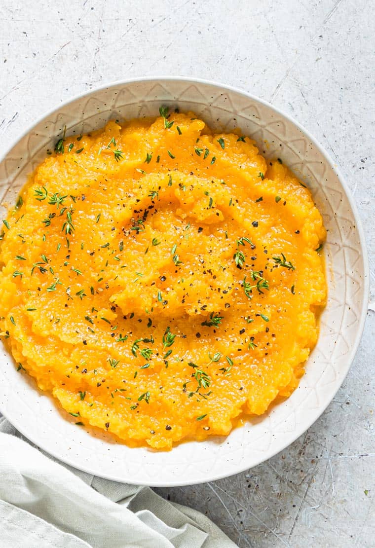 Mashed butternut squash with green garnish in a white bowl.
