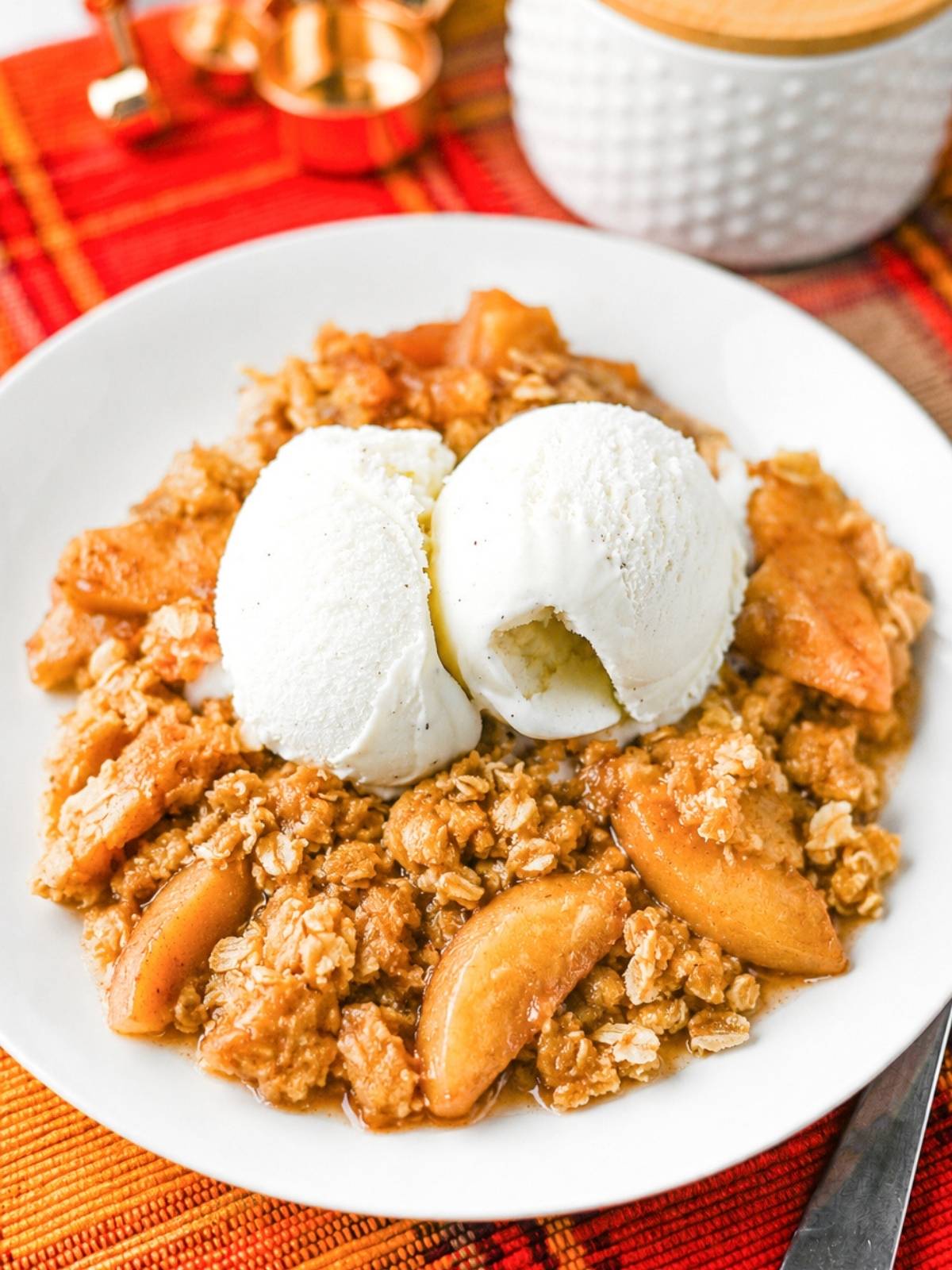 Apple crisp on a white plate with two scoops of vanilla ice cream on top,