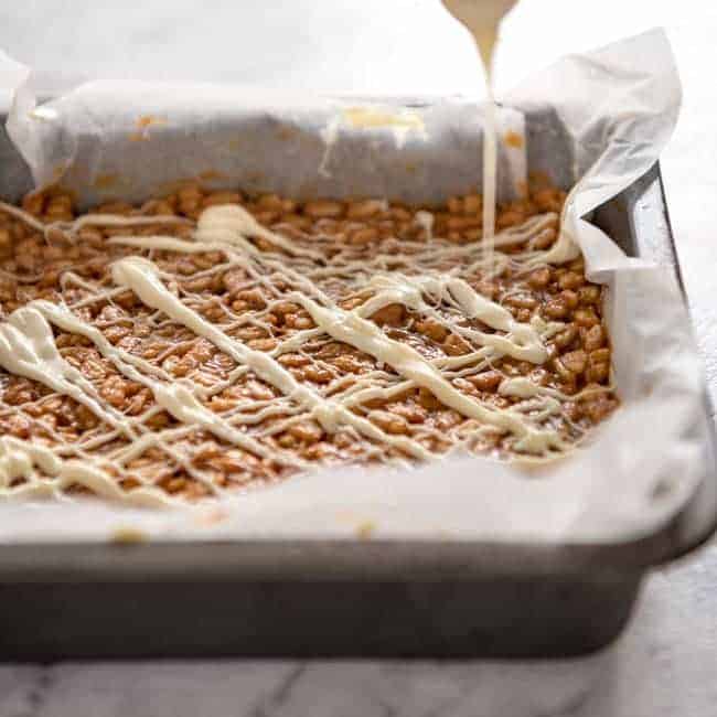 Dulce de leche rice Krispies with glaze in a parchment lined baking pan.