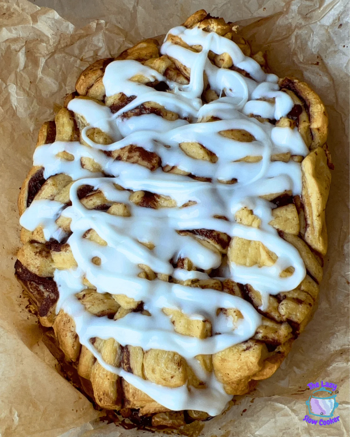 Crockpot monkey bread with cream cheese frosting on brown parchment paper.