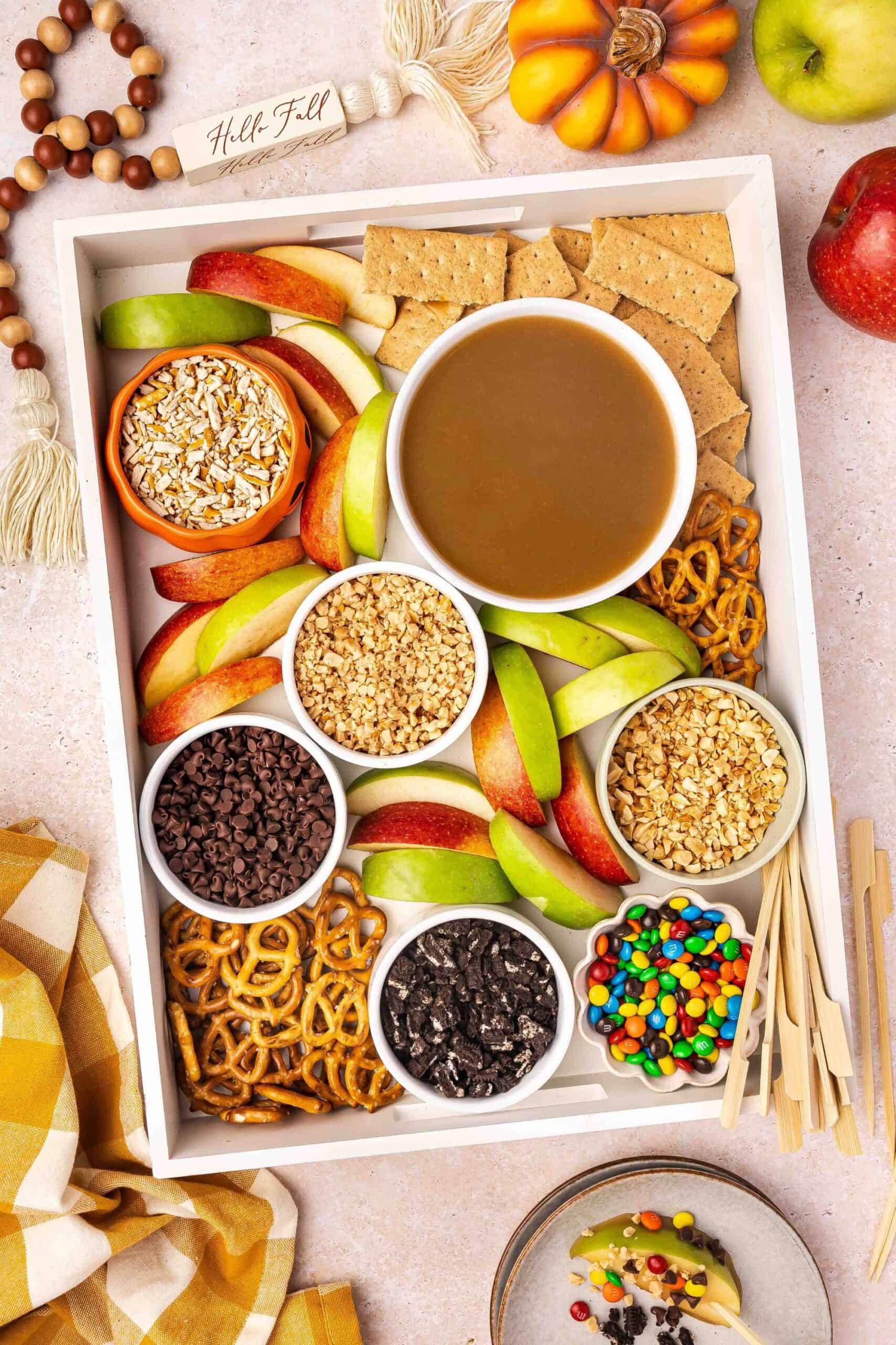 Caramel dip charcuterie board with apples, nuts, and chocolate chips.