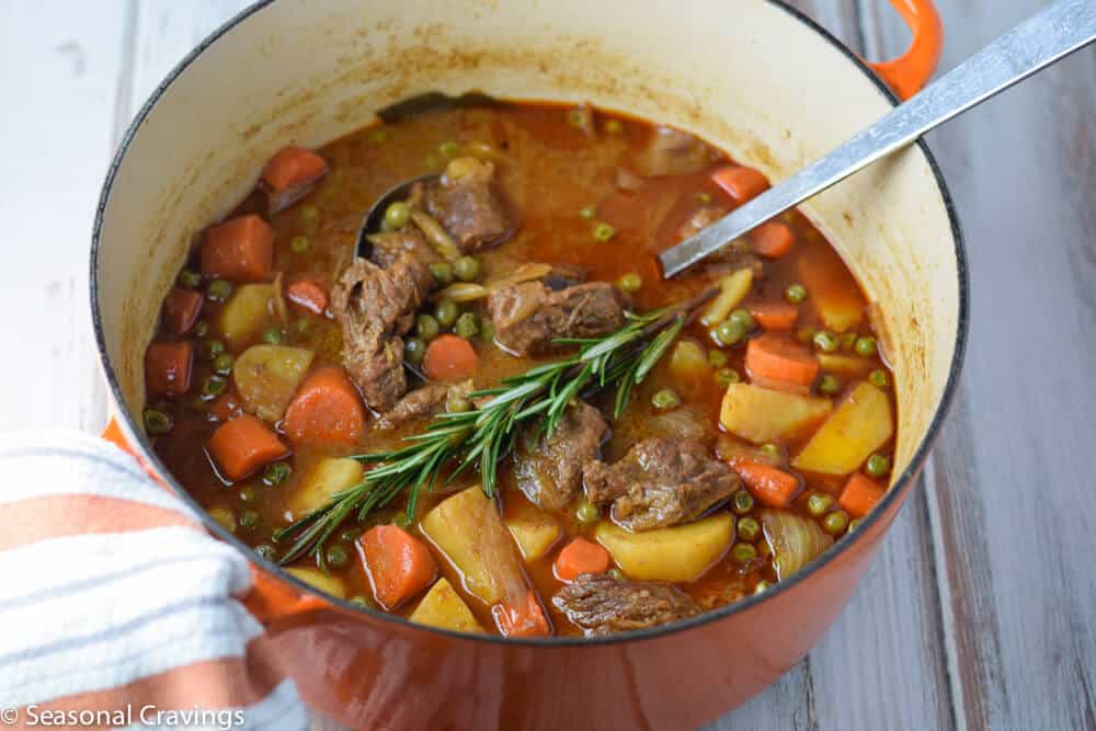 A Dutch oven filled with apple cider beef stew with carrots and potatoes.