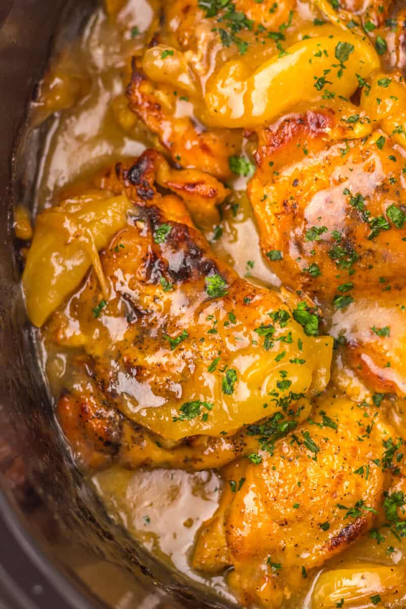 Smothered chicken and apples in a crockpot with green garnish on top.