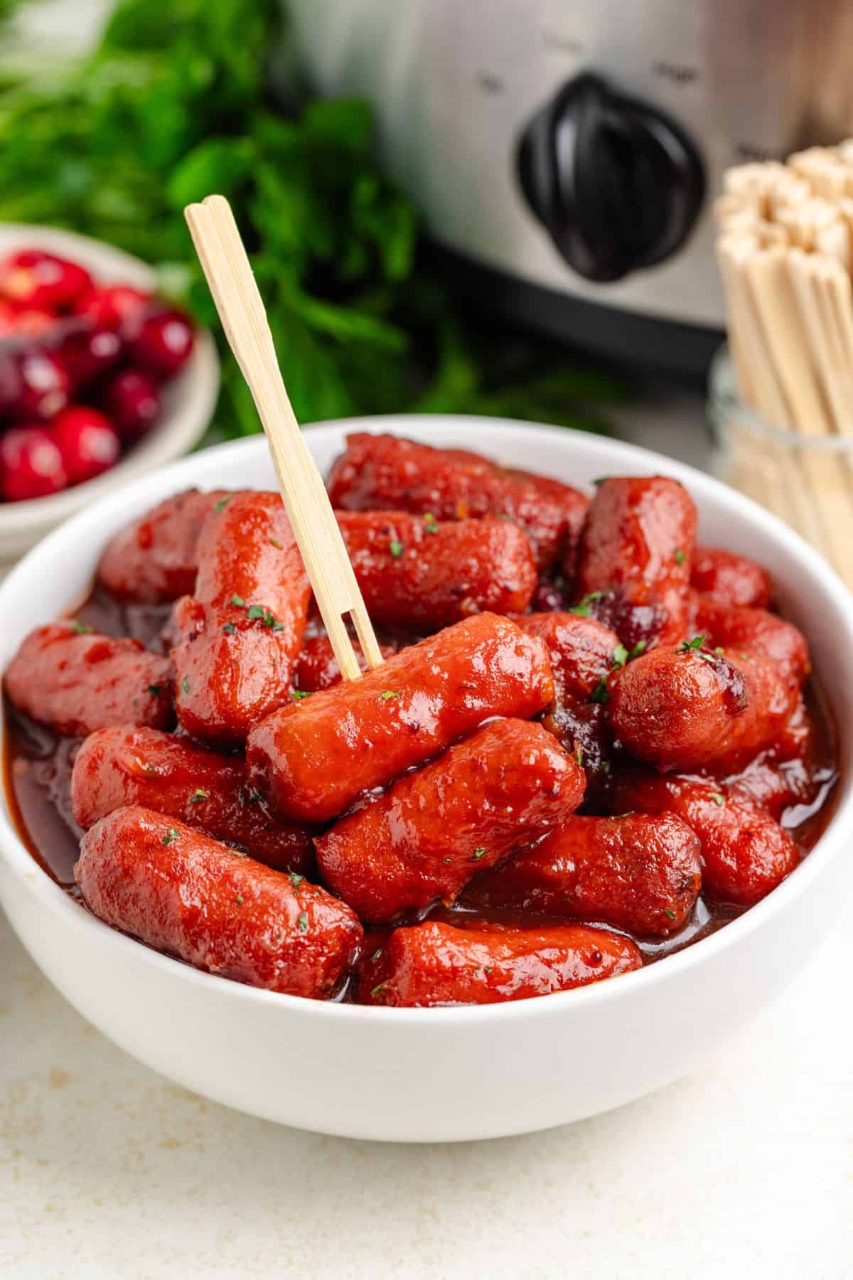 Cranberry little smokies in a small white bowl with a cocktail pick.