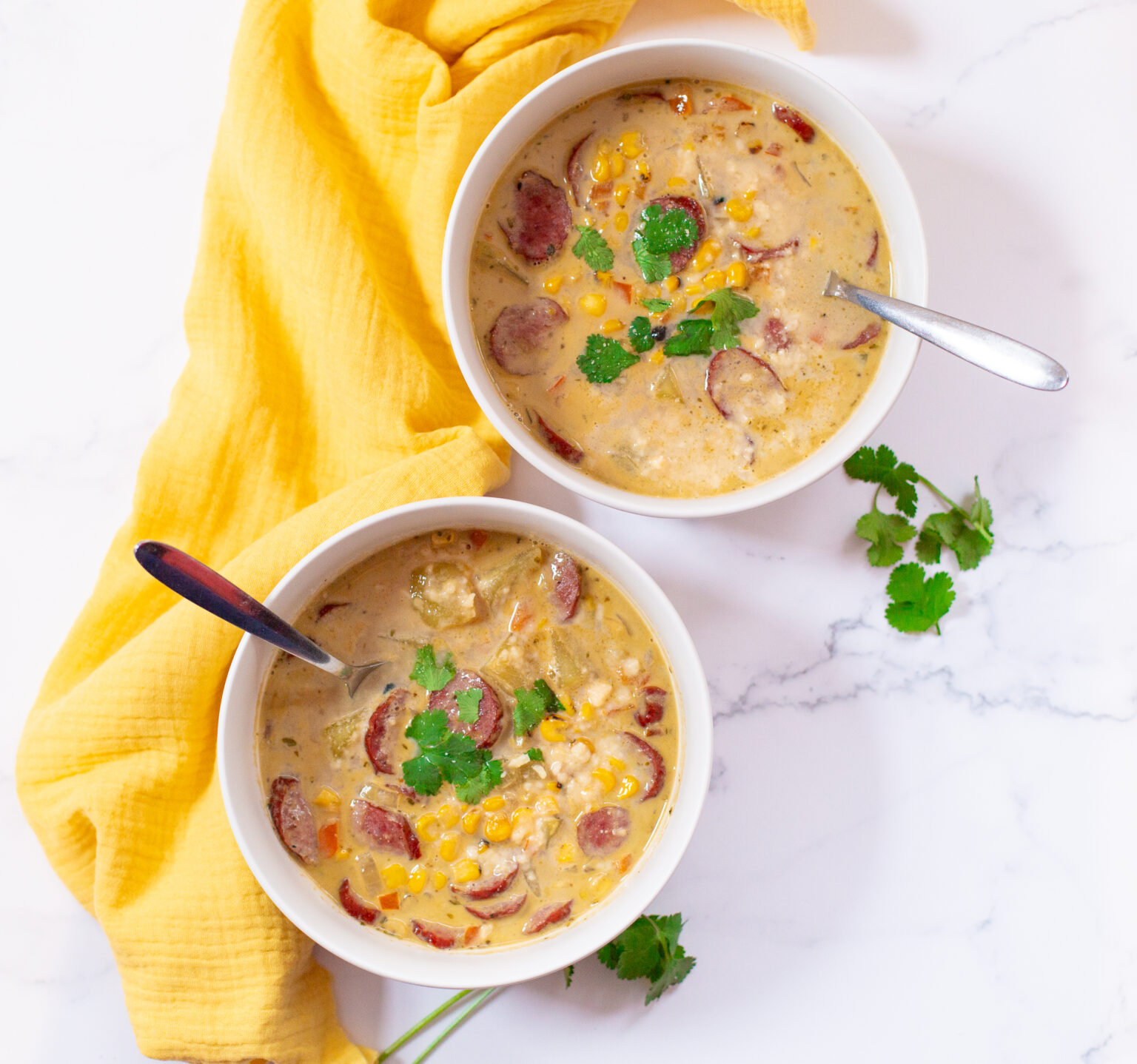 Chicken corn chowder in two white bowls next to a yellow kitchen towel.