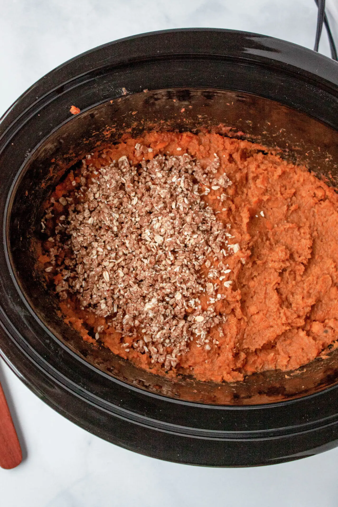 Sweet potato casserole half topped with crumble topping in a black crockpot.