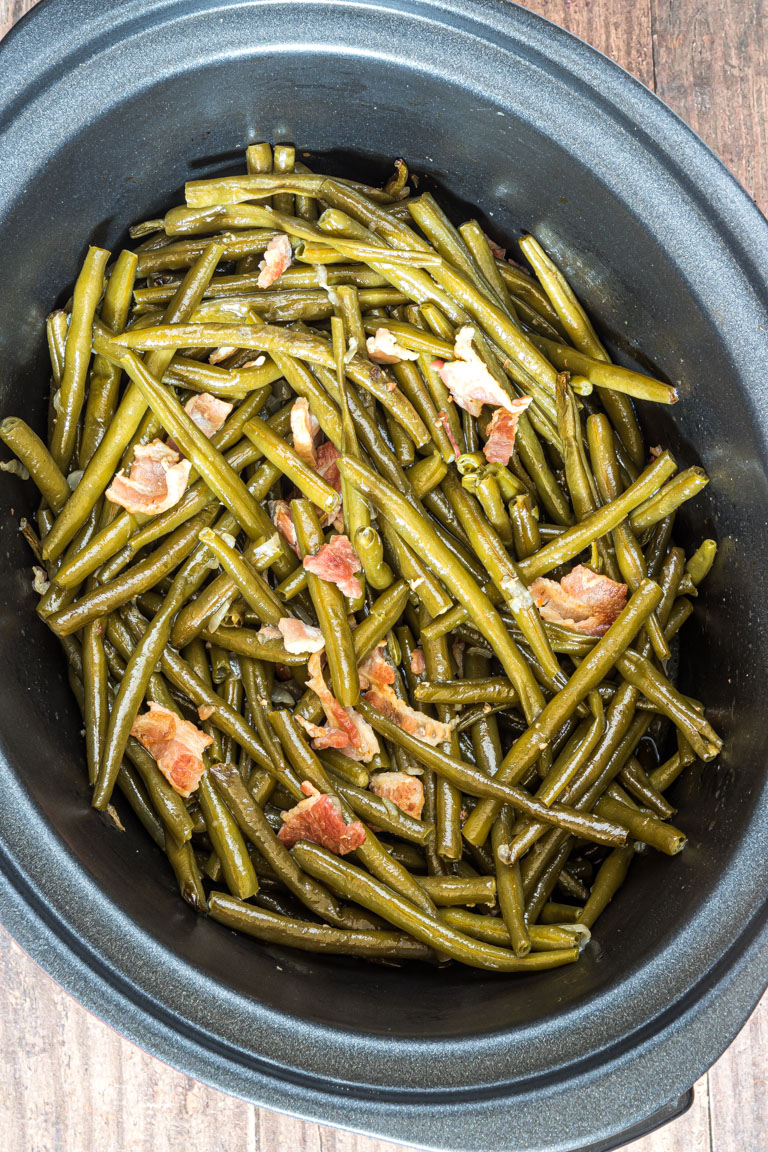 Green beans and bacon in a large black crockpot base.