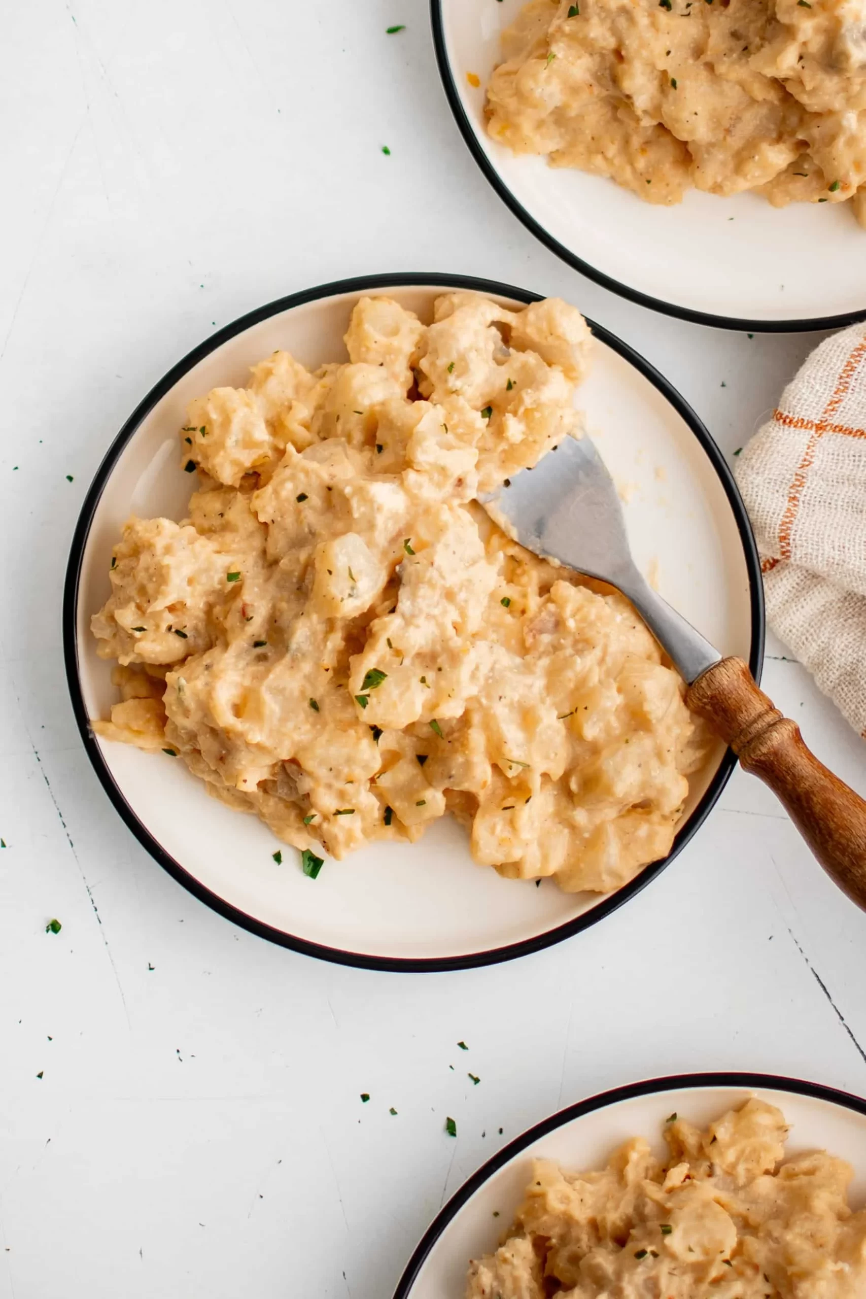 Cheesy potatoes on three plates next to a orange checkered kitchen towel.