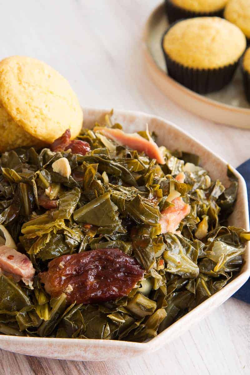Collard greens in a cream bowl with smoked turkey meat and a cornbread muffin.