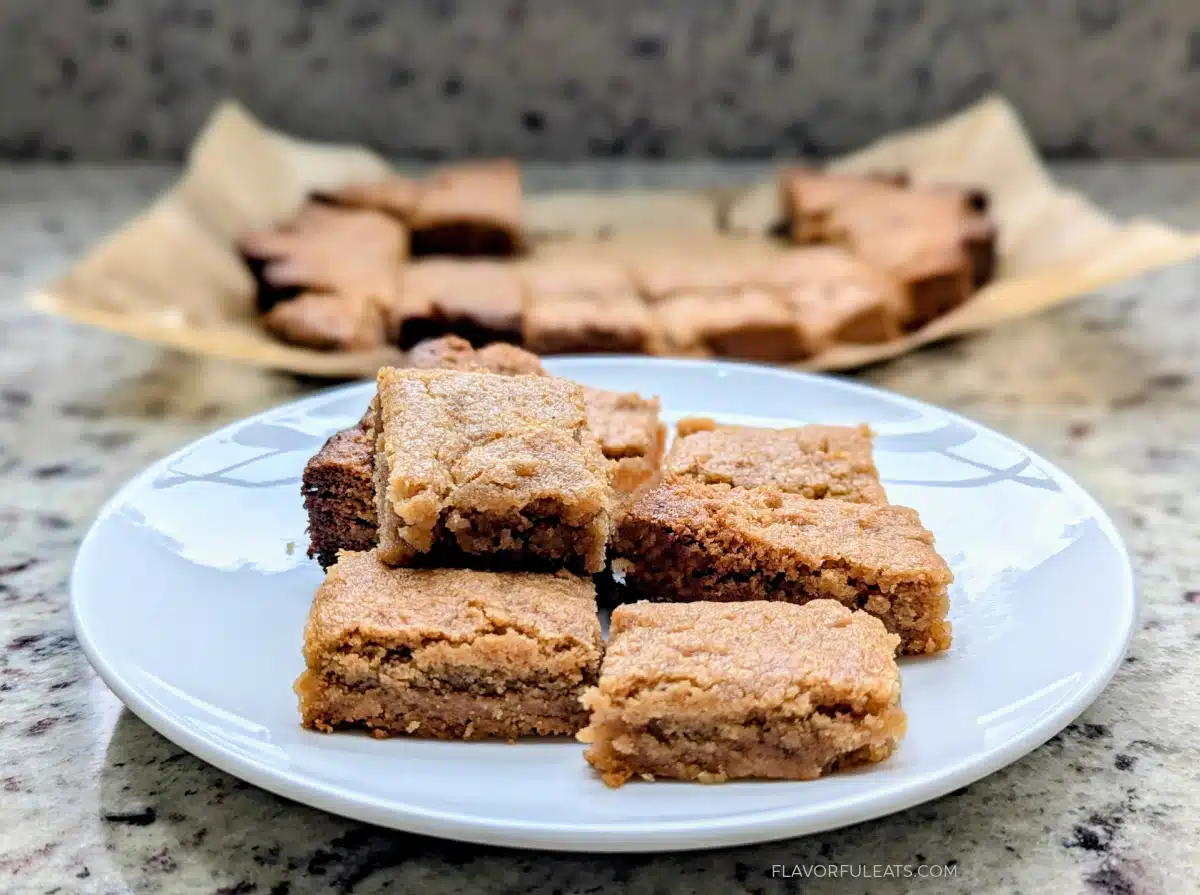 A stack of brown cookie bars on a white plate with more in the background on parchment paper.