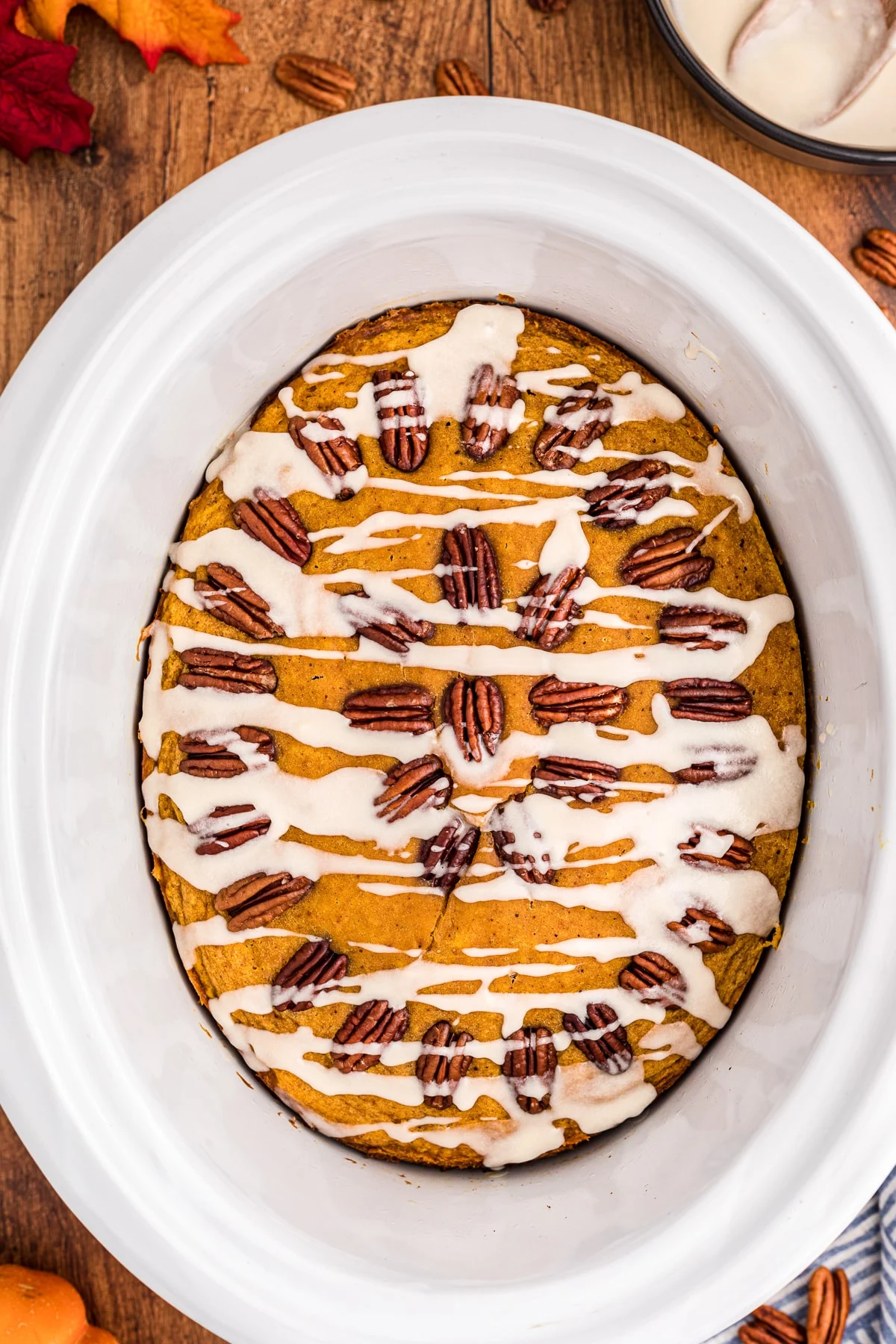 Crockpot pumpkin spoon cake with pecans and white glaze drizzled on top.