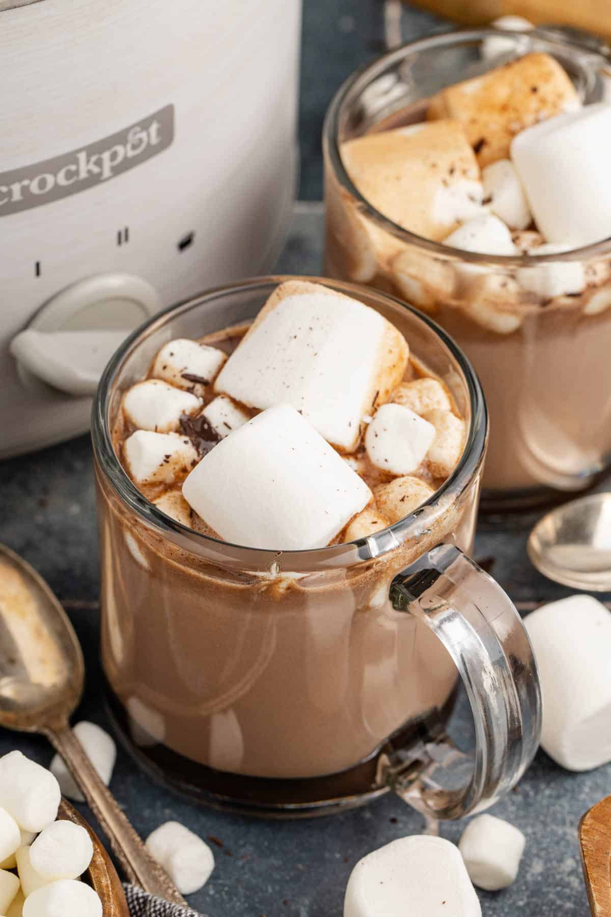 Crockpot hot chocolate in two clear mugs with jumbo and mini marshmallows on top.