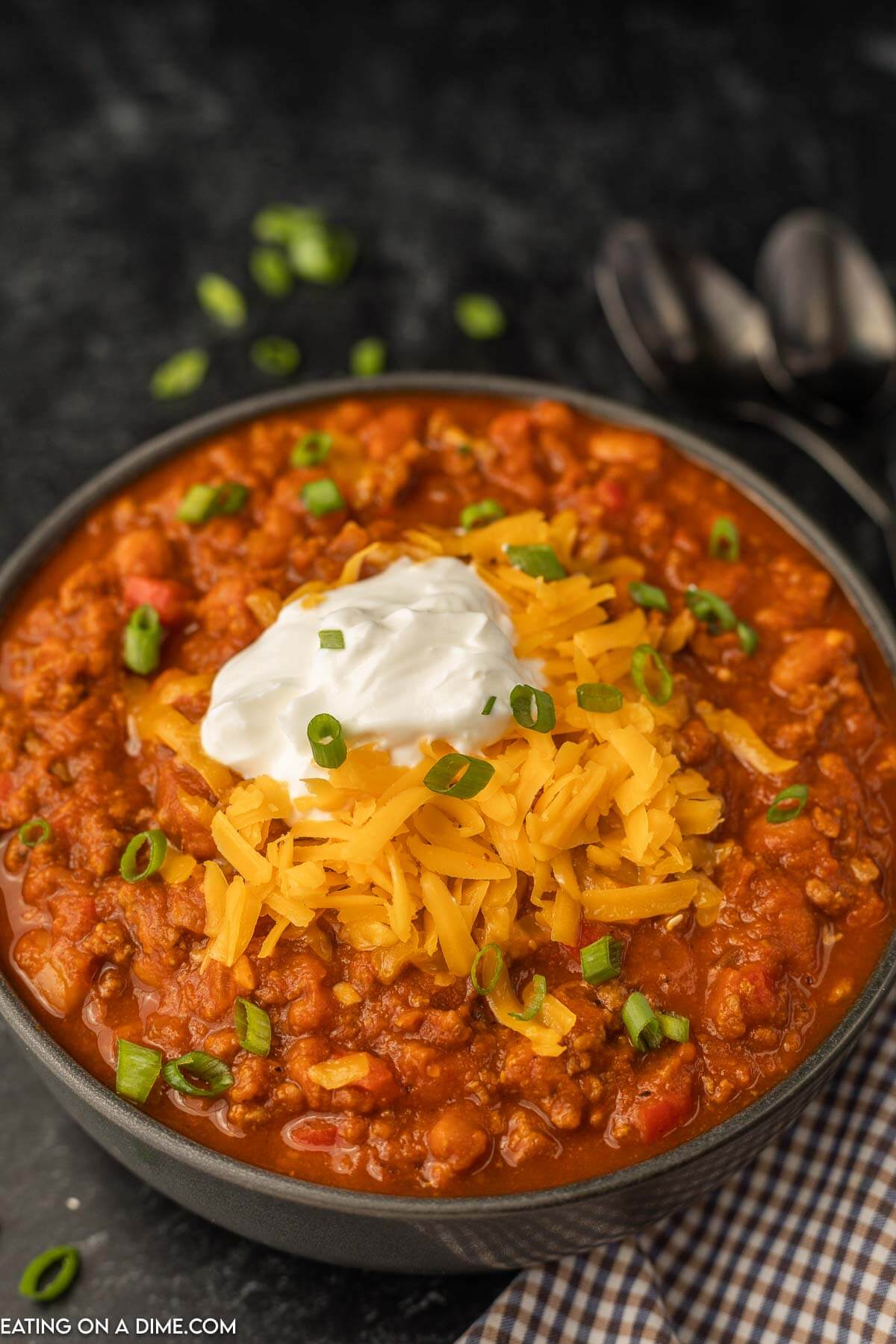 Pumpkin chili in a black bowl with sour cream, shredded cheese, and green garnish on top.