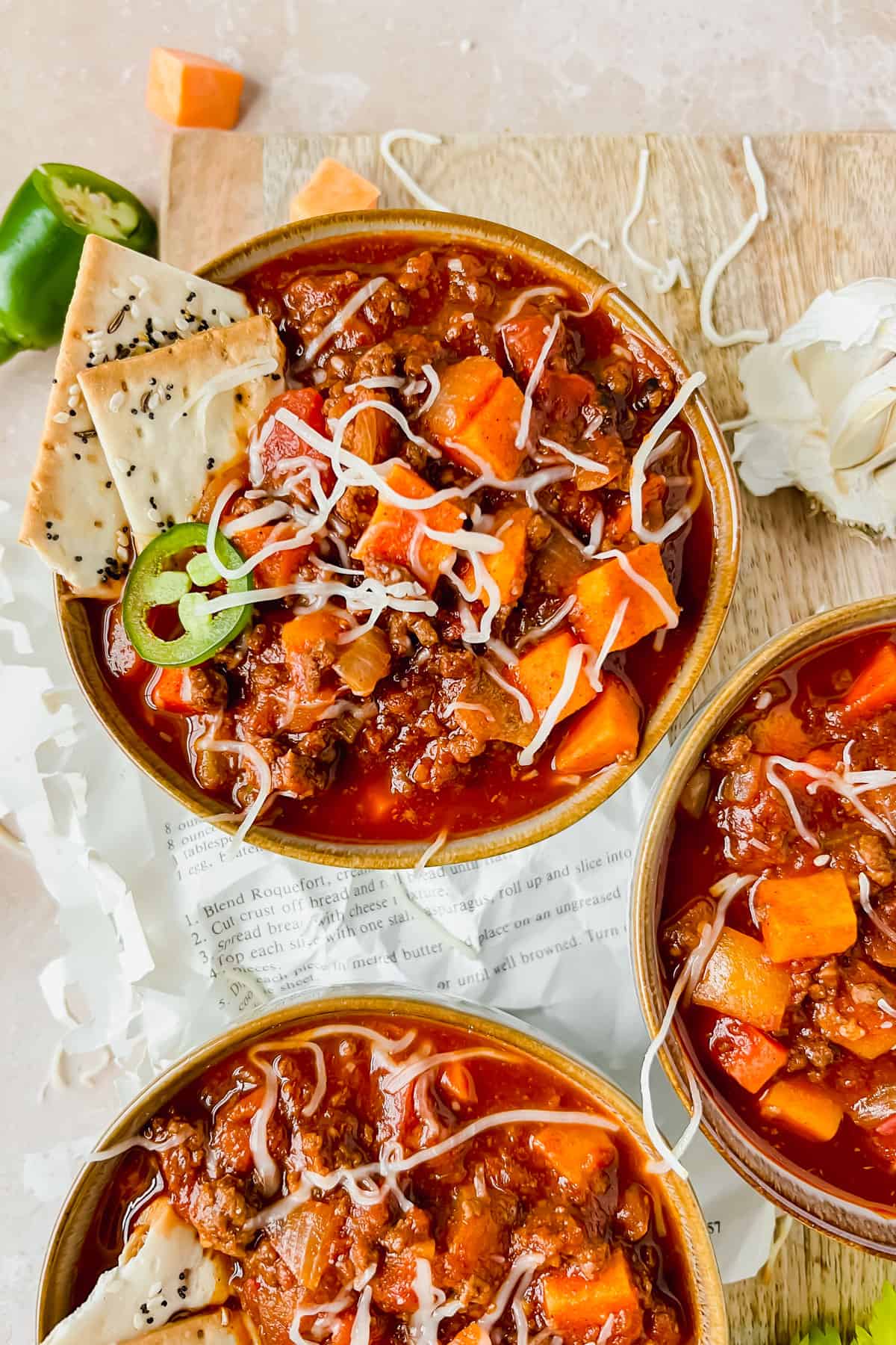 Harvest chili with sweet potatoes in three bowls with white cheese and crackers on top.